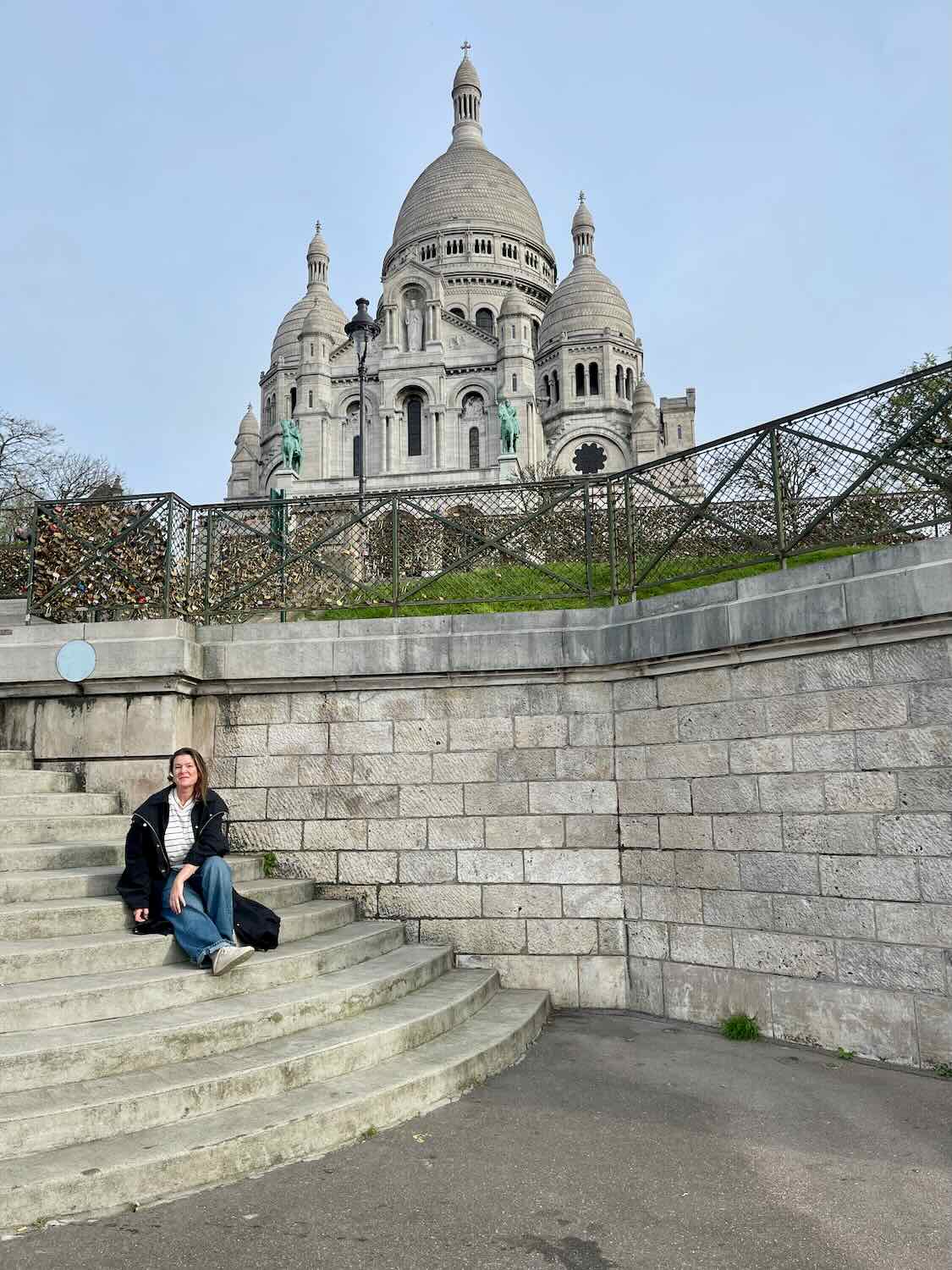 A woman sitting alone on the steps in Paris in front of a large church. 