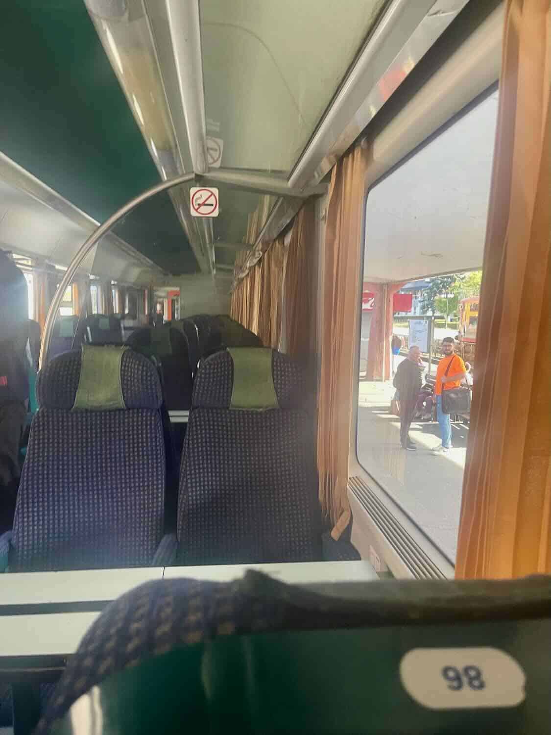 Interior view of a Romanian train carriage with patterned seats and large windows showing a view of the platform, capturing the experience of travel by rail