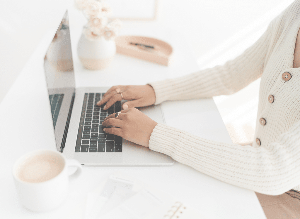 Close-up of a woman typing on a laptop in a bright and minimalist workspace, planning a trip using ChatGPT for travel planning.