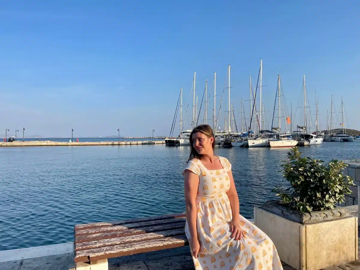 a solo woman in her 30s sitting on a bench at the harbor